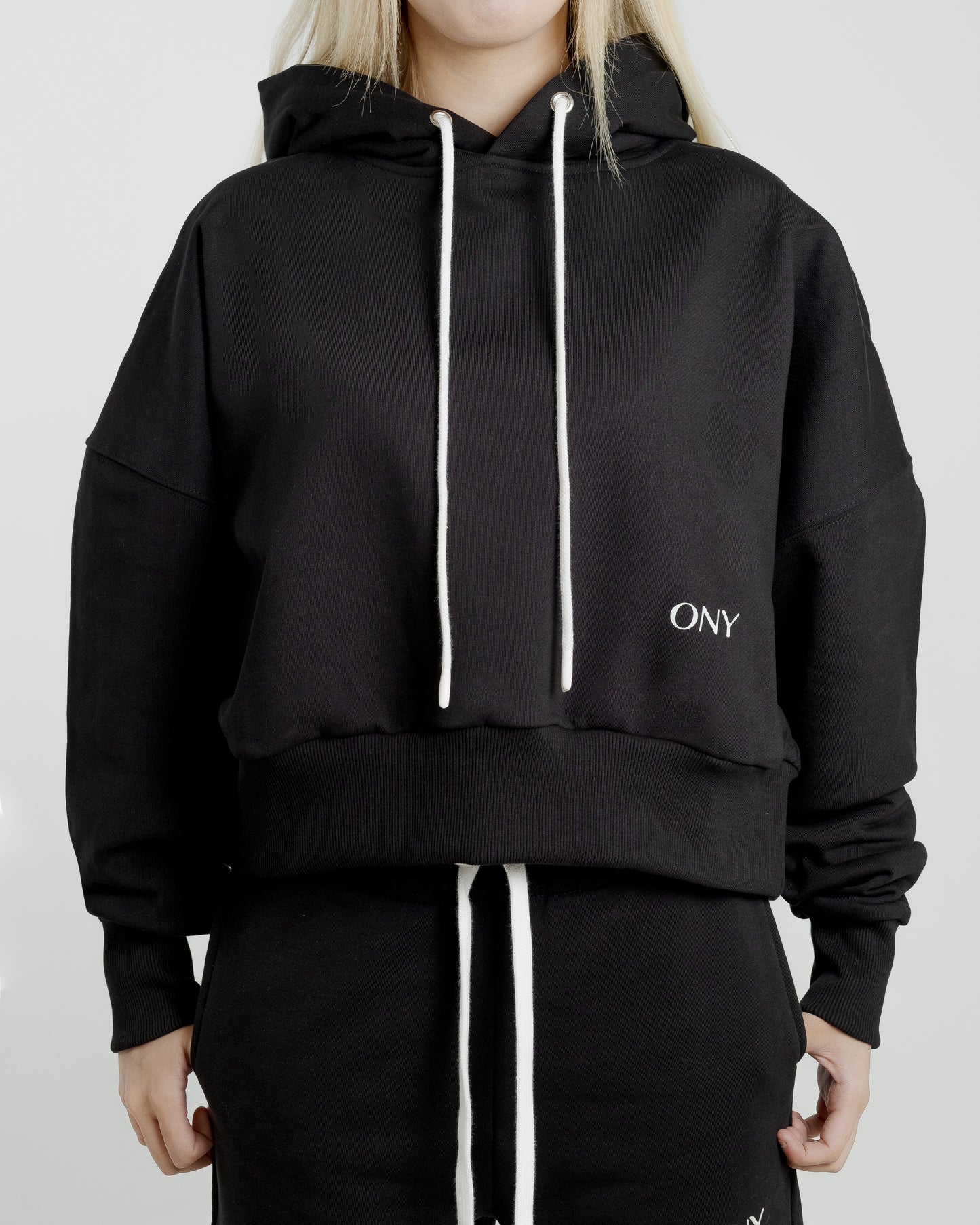 A female model showcasing our black cropped hoodie, styled with a slightly oversized fit and a modern cropped silhouette waist, perfect for a trendy and relaxed look.