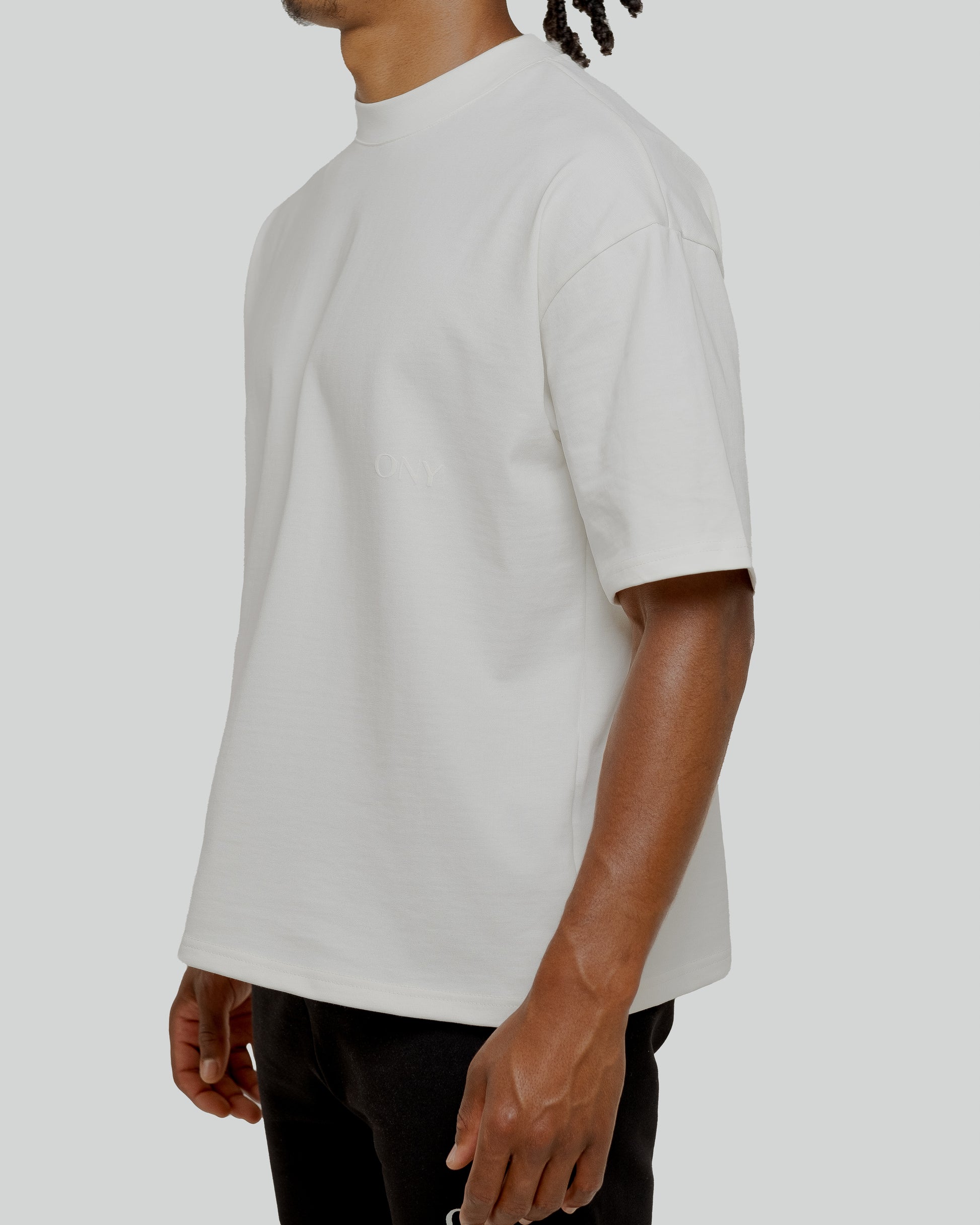 A male model wearing our off-white oversized tee with a slightly cropped body length and a boxy fit.