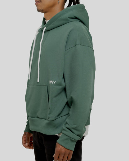 A male model showcasing our green dropped shoulder hoodie with a slight cropped body length, designed for trendy and versatile layering looks