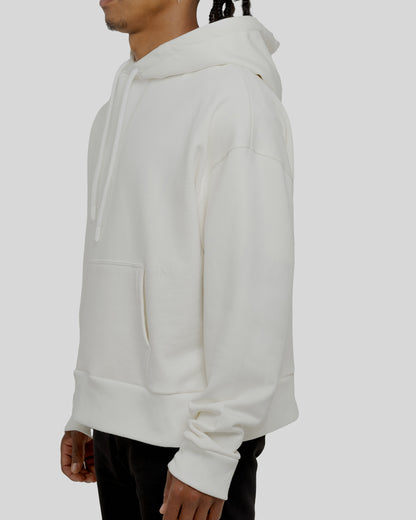 A male model showcasing our off-white dropped shoulder hoodie with a slight cropped body length, designed for trendy and versatile layering looks