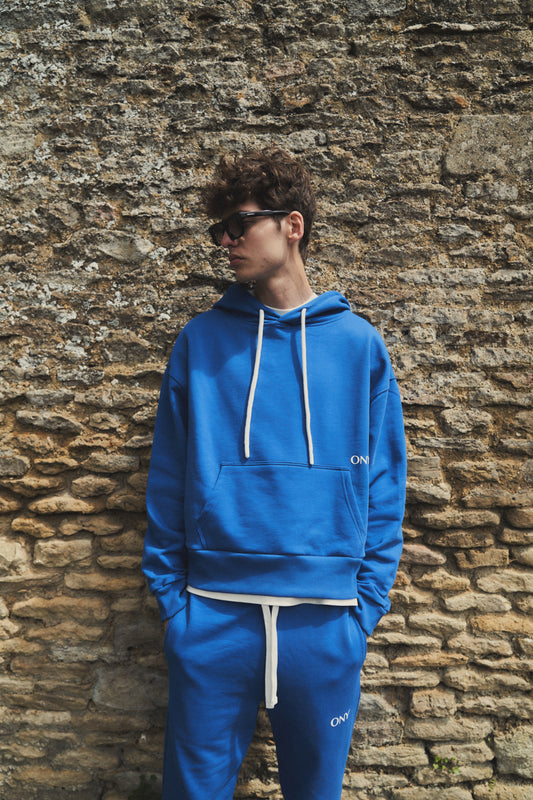 A male model showcasing our blue dropped shoulder hoodie with a slight cropped body length, designed for trendy and versatile layering looks, styled with our blue split sweatpants for a laid-back yet fashionable look. 