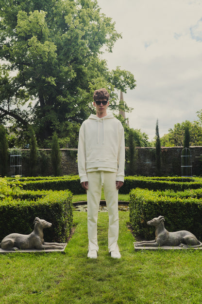 A male model showcasing our off-white dropped shoulder hoodie with a slight cropped body length, designed for trendy and versatile layering looks, styled with our off-white split sweatpants for a laid-back yet fashionable look. 