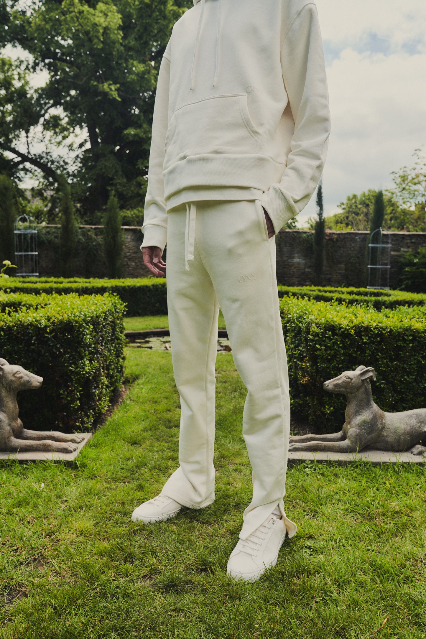 A male model showcasing our off-white dropped shoulder hoodie with a slight cropped body length, designed for trendy and versatile layering looks, styled with our off-white split sweatpants for a laid-back yet fashionable look. 