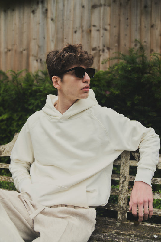 A male model wearing a stylish off white oversized hoodie, perfect for a comfortable and fashionable look.  
