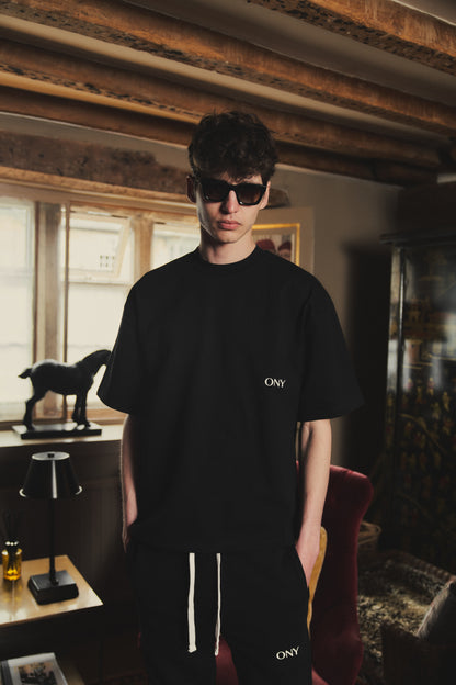 A male model wearing our Black oversized tee with a slightly cropped body length and a boxy fit, styled with our black split sweatpants for a laid-back yet fashionable look.