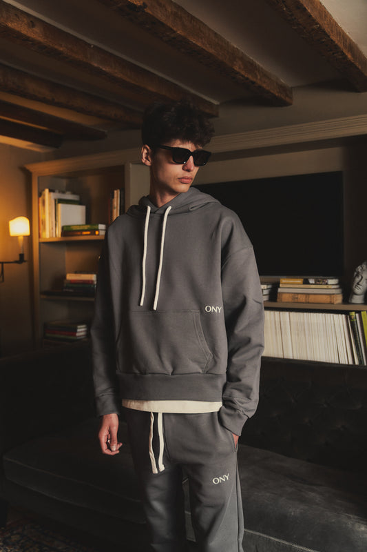 A male model showcasing our grey dropped shoulder hoodie with a slight cropped body length, designed for trendy and versatile layering looks, styled with our grey sweatpants for a laid-back yet fashionable look. 