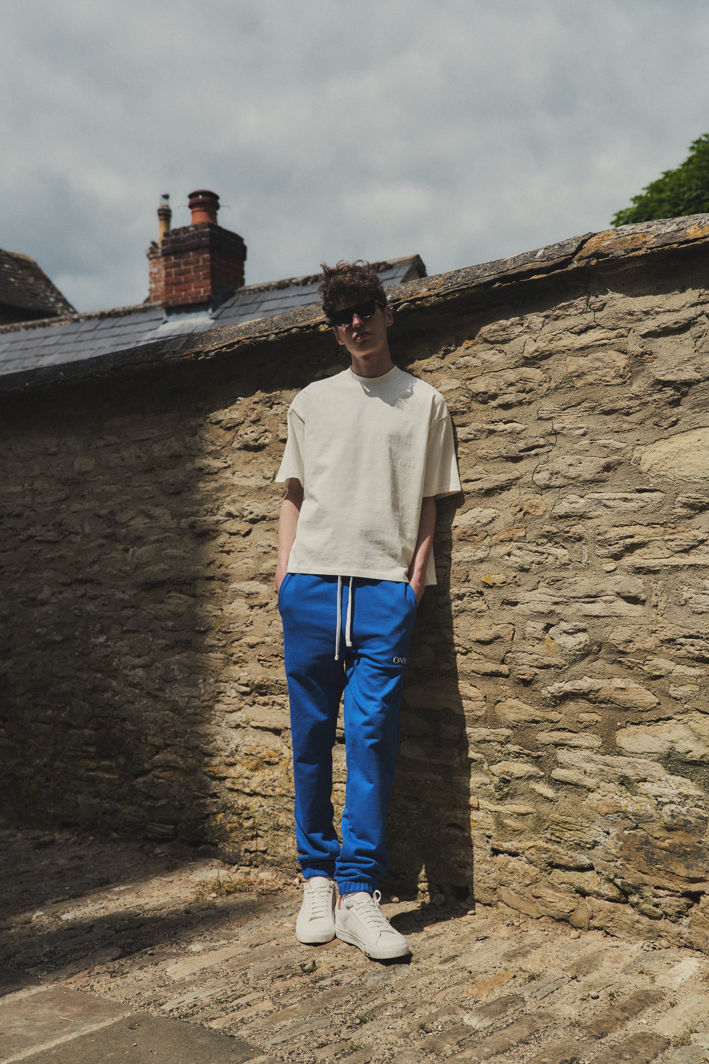 A male model wearing our off-white oversized tee with a slightly cropped body length and a boxy fit, styled with our blue sweatpants for a laid-back yet fashionable look.