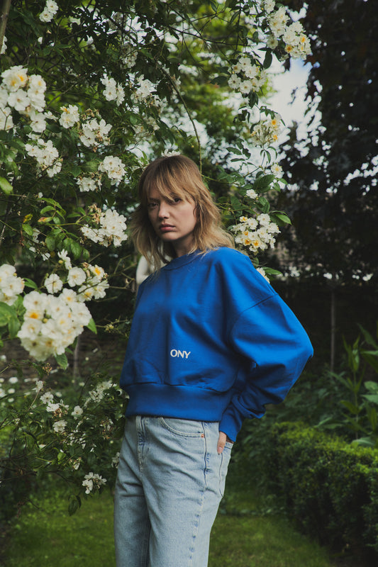 A female model wearing our blue women's cropped sweatshirt, featuring a slightly oversized fit and a trendy cropped style above the waist, perfect for a fashion-forward and casual ensemble.