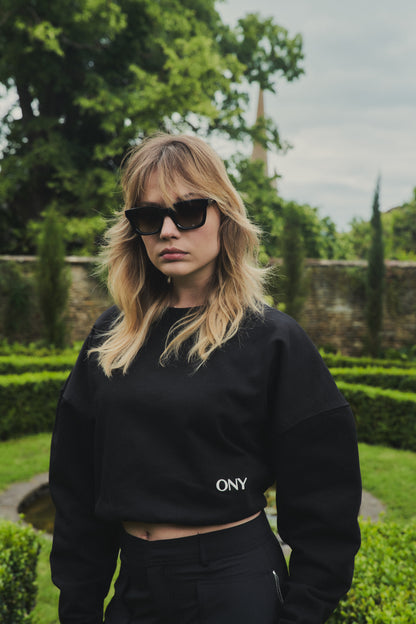 A female model wearing our black women's cropped sweatshirt, featuring a slightly oversized fit and a trendy cropped style above the waist, perfect for a fashion-forward and casual ensemble.