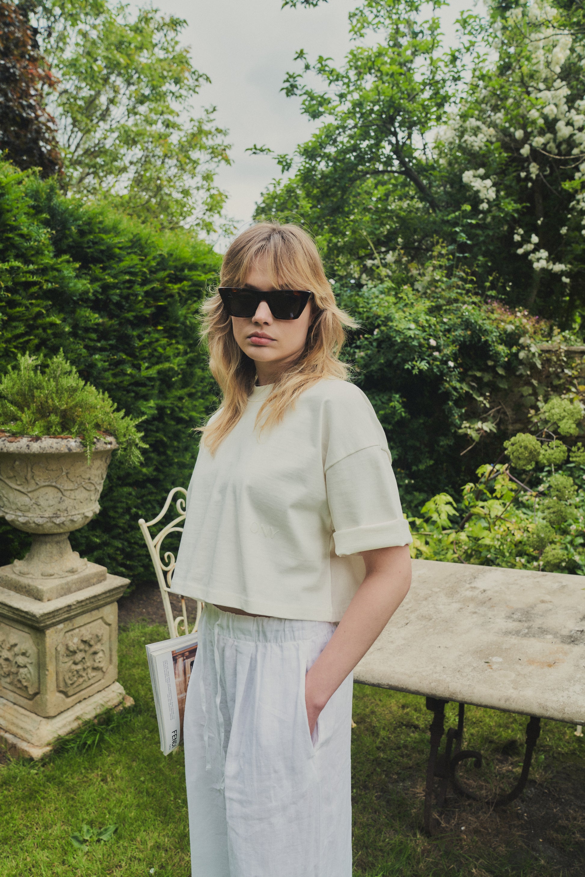 A female model in our women's off-white cropped tee, featuring a boxy fit and cropped above the waist for a stylish and relaxed look.