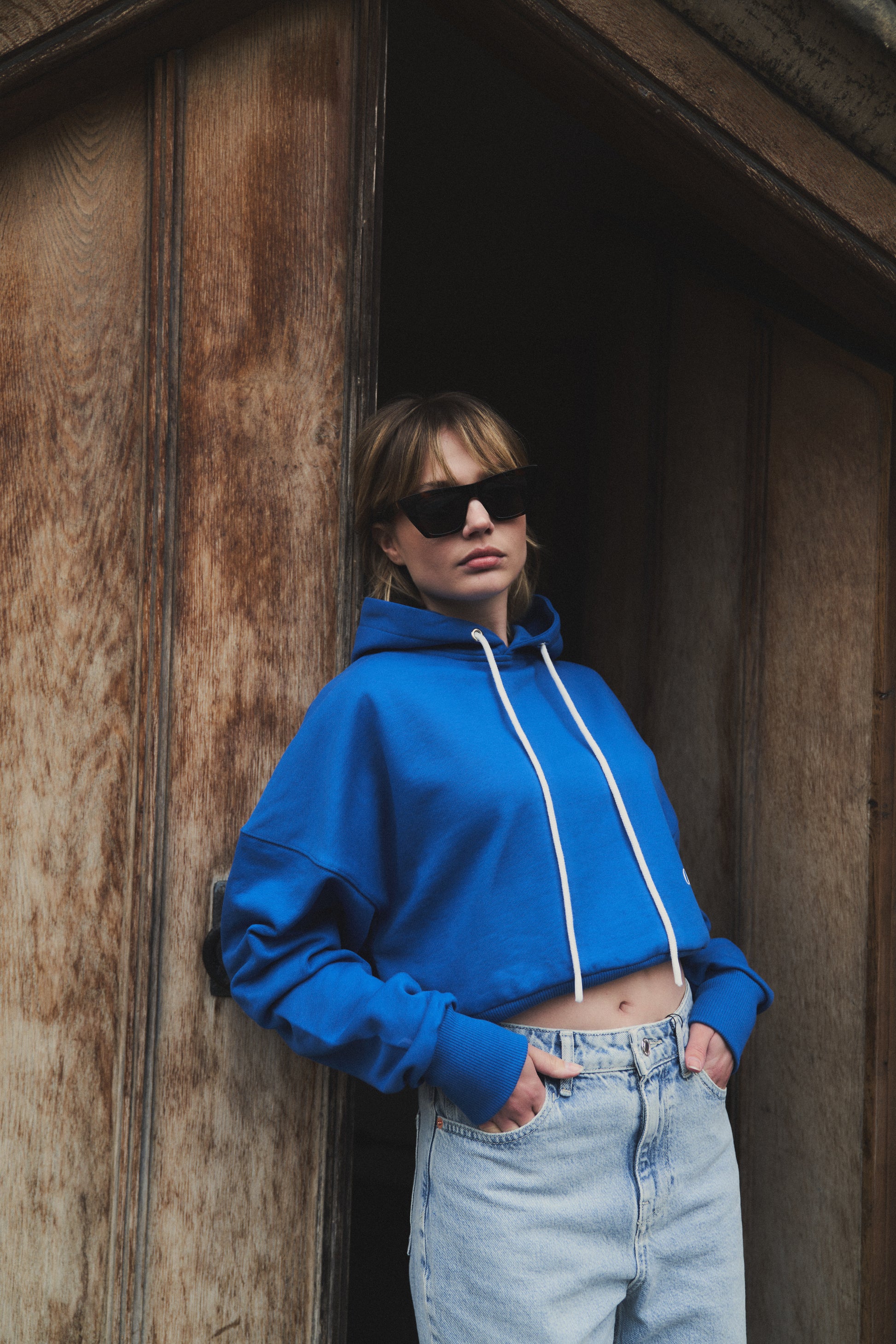 A female model showcasing our blue cropped hoodie, styled with a slightly oversized fit and a modern cropped silhouette waist, perfect for a trendy and relaxed look. 