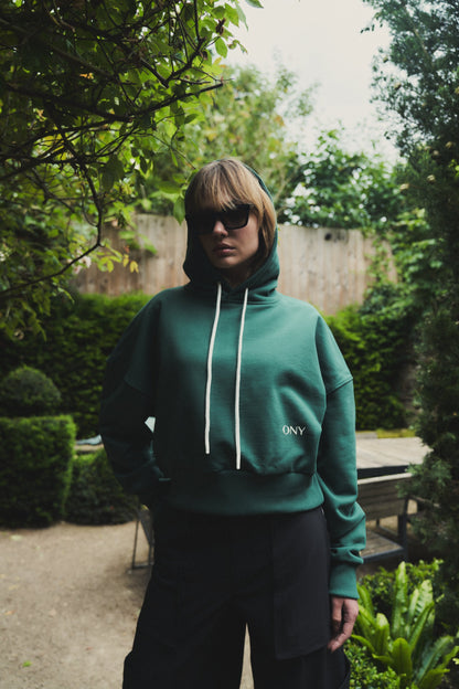 A female model showcasing our green cropped hoodie, styled with a slightly oversized fit and a modern cropped silhouette waist, perfect for a trendy and relaxed look. 