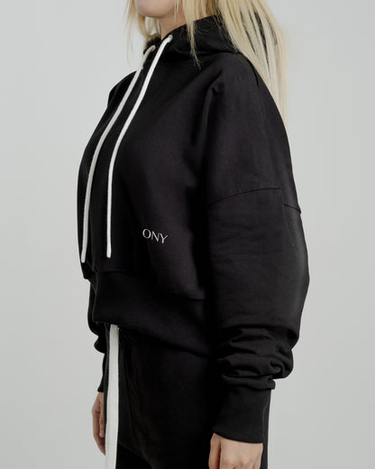 A female model showcasing our black cropped hoodie, styled with a slightly oversized fit and a modern cropped silhouette waist, perfect for a trendy and relaxed look. 