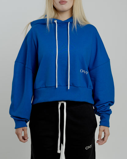 A female model showcasing our blue cropped hoodie, styled with a slightly oversized fit and a modern cropped silhouette waist, perfect for a trendy and relaxed look. 