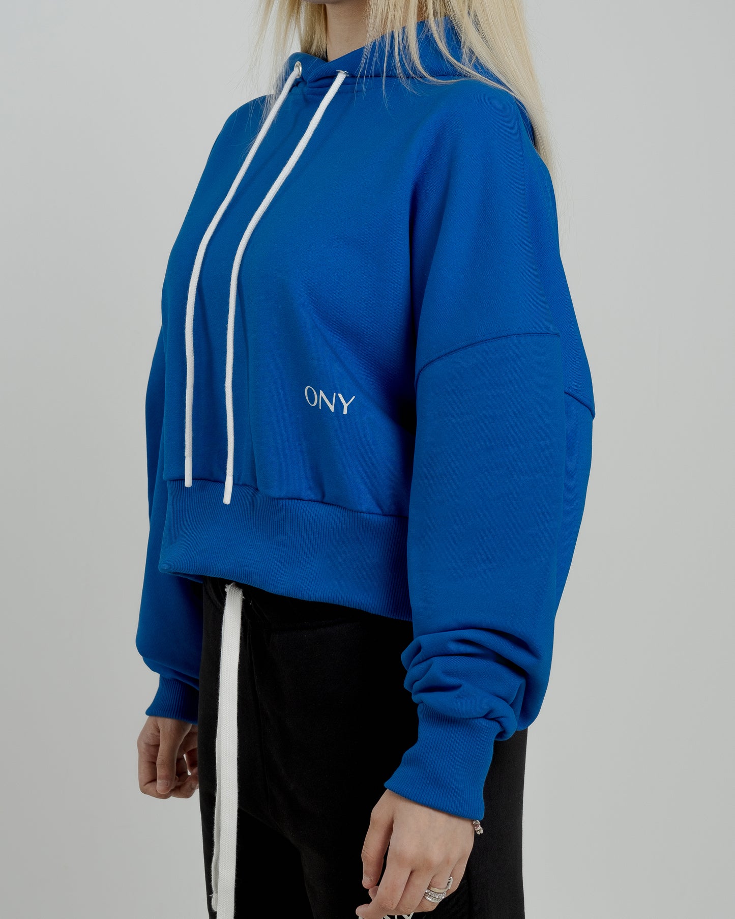 A female model showcasing our blue cropped hoodie, styled with a slightly oversized fit and a modern cropped silhouette waist, perfect for a trendy and relaxed look. 