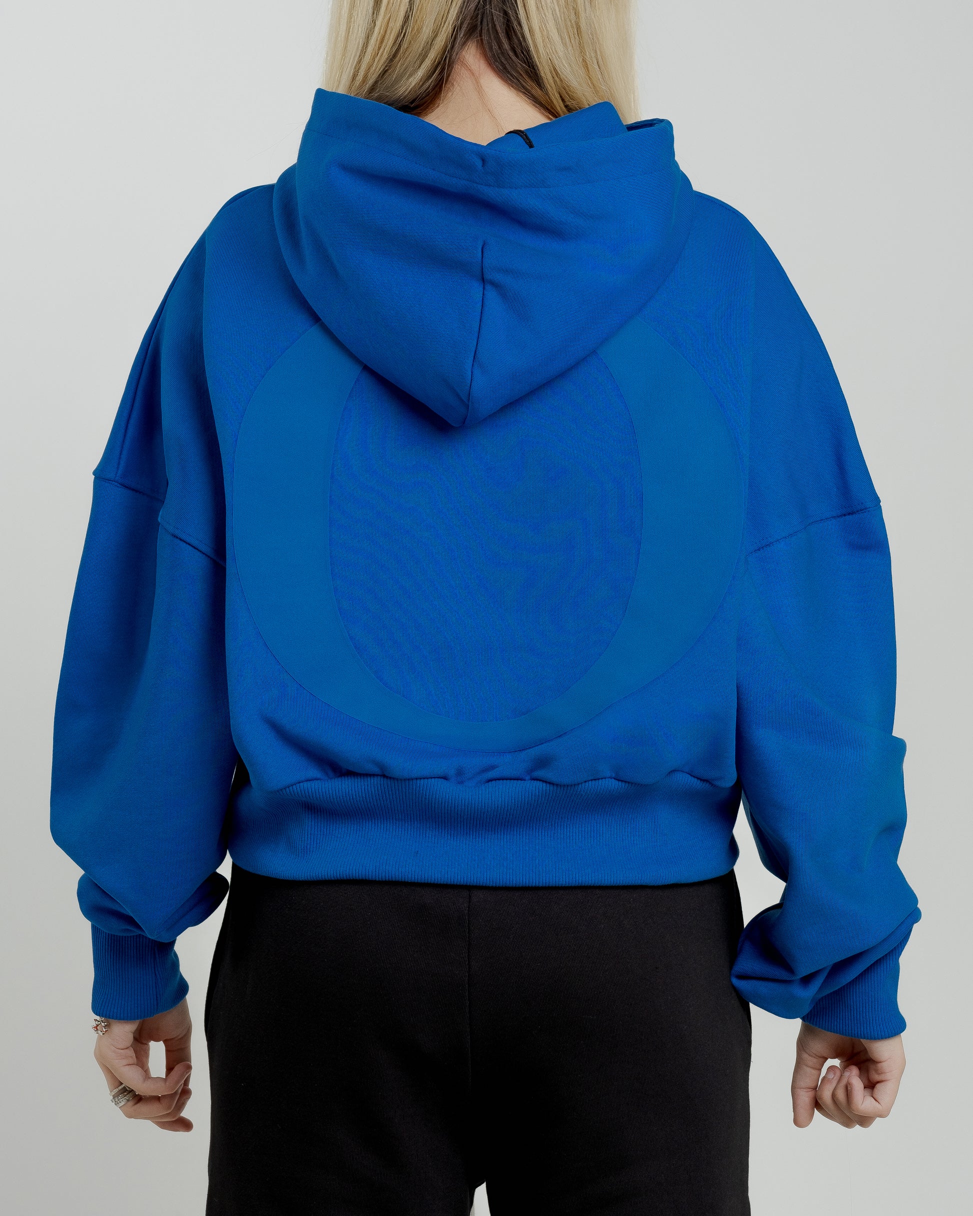 A female model showcasing our blue cropped hoodie, styled with a slightly oversized fit and a modern cropped silhouette waist, perfect for a trendy and relaxed look. 