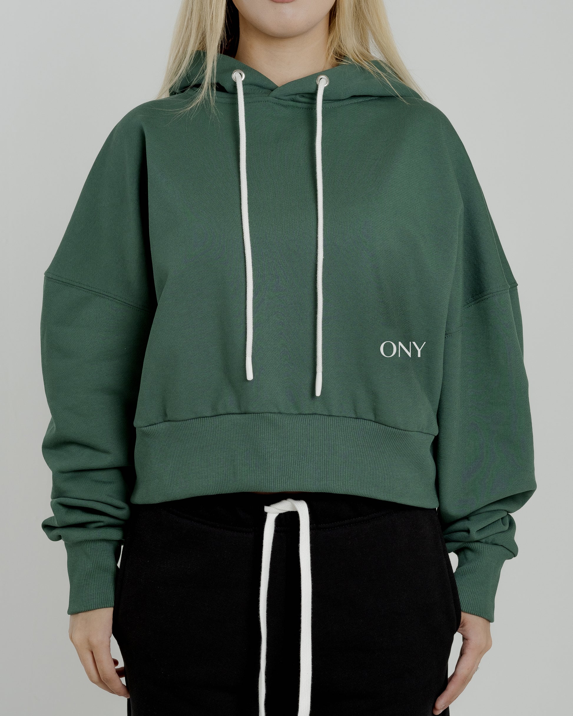 A female model showcasing our green cropped hoodie, styled with a slightly oversized fit and a modern cropped silhouette waist, perfect for a trendy and relaxed look. 