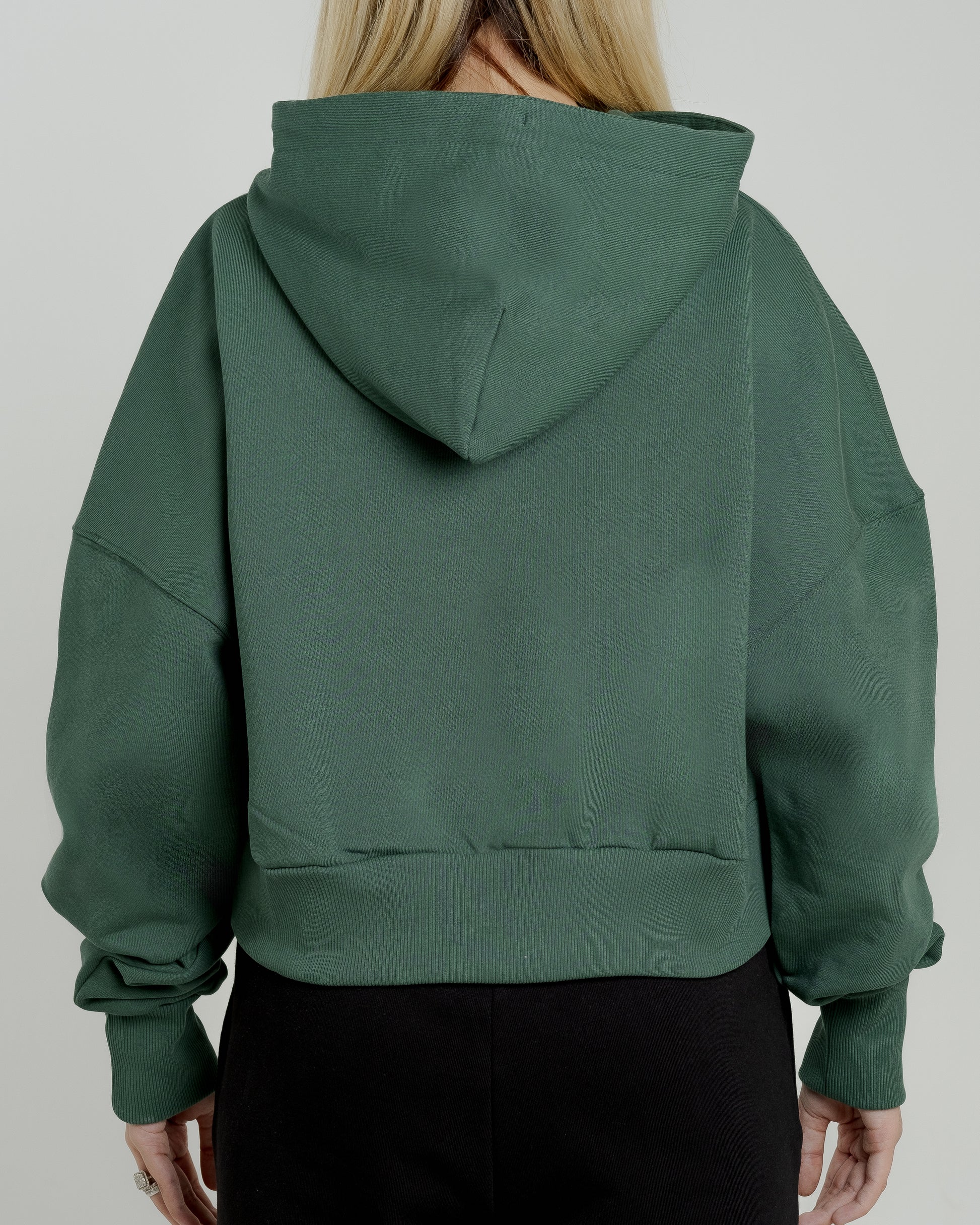 A female model showcasing our green cropped hoodie, styled with a slightly oversized fit and a modern cropped silhouette waist, perfect for a trendy and relaxed look. 