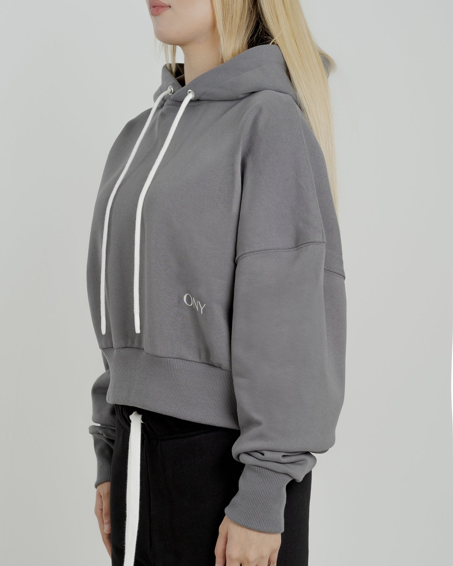 A female model showcasing our grey cropped hoodie, styled with a slightly oversized fit and a modern cropped silhouette waist, perfect for a trendy and relaxed look. 