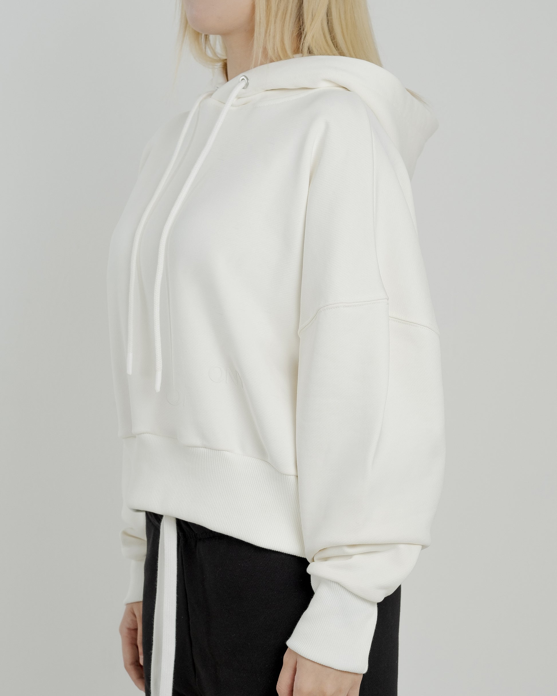 A female model showcasing our off-white cropped hoodie, styled with a slightly oversized fit and a modern cropped silhouette waist, perfect for a trendy and relaxed look. 